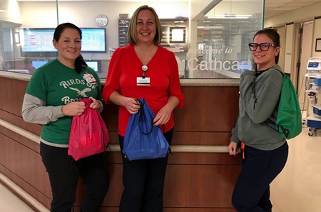 Three staff members at a nurses station posing with drawstring bags
